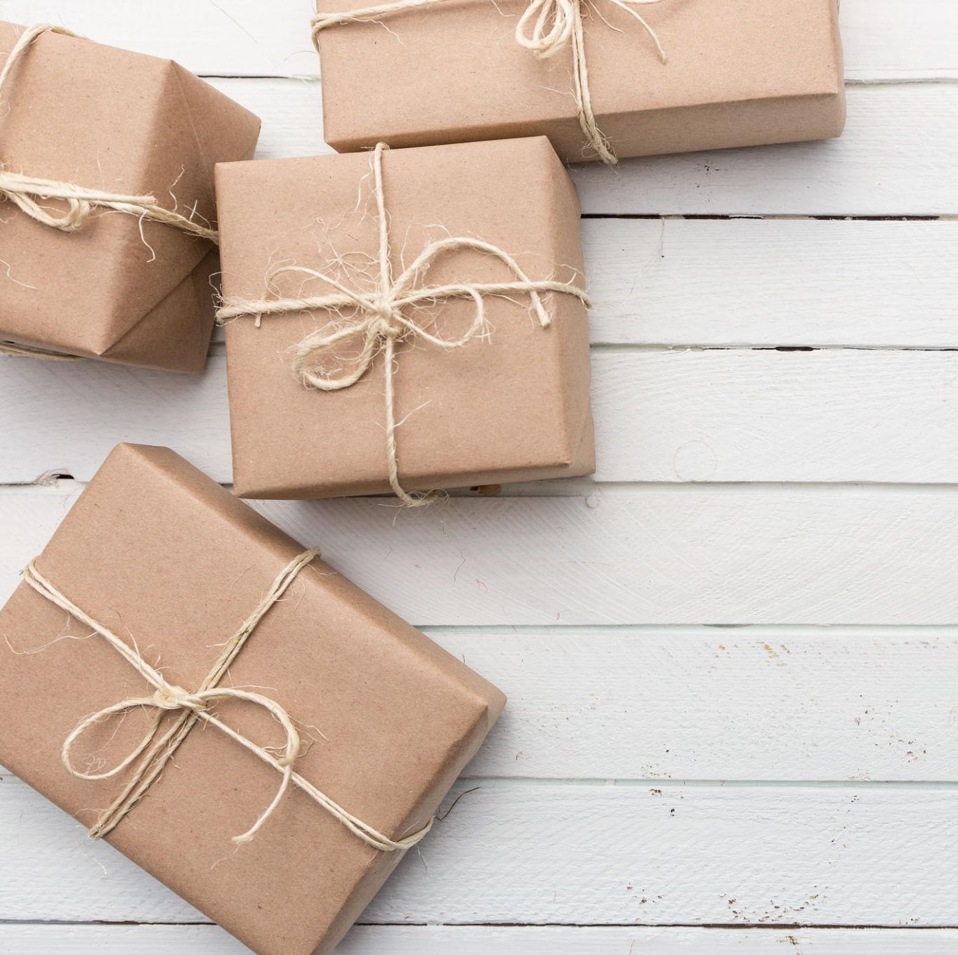 Four brown paper-wrapped gifts with string ties on a light wooden surface