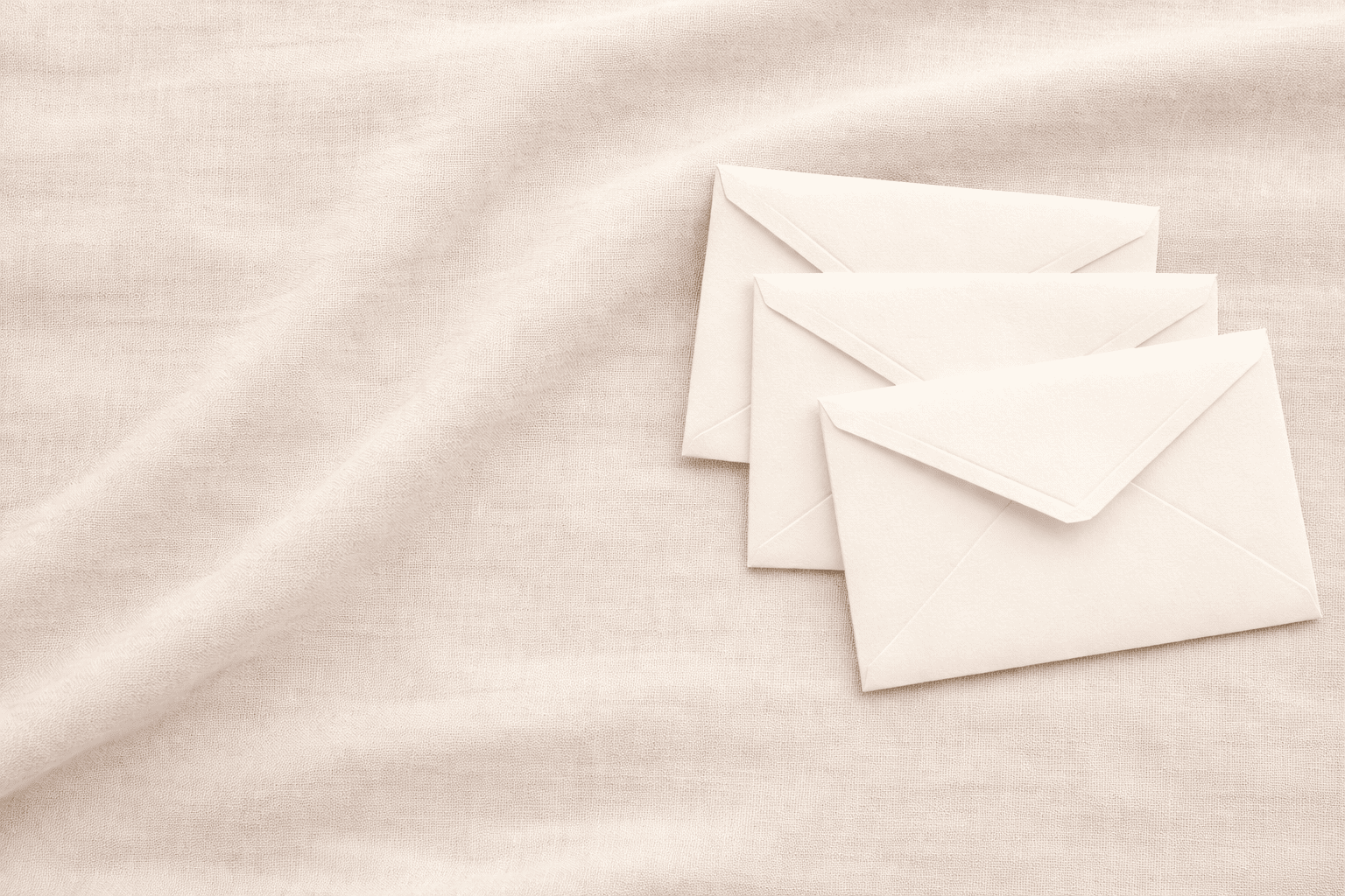 Three white envelopes on a beige fabric background