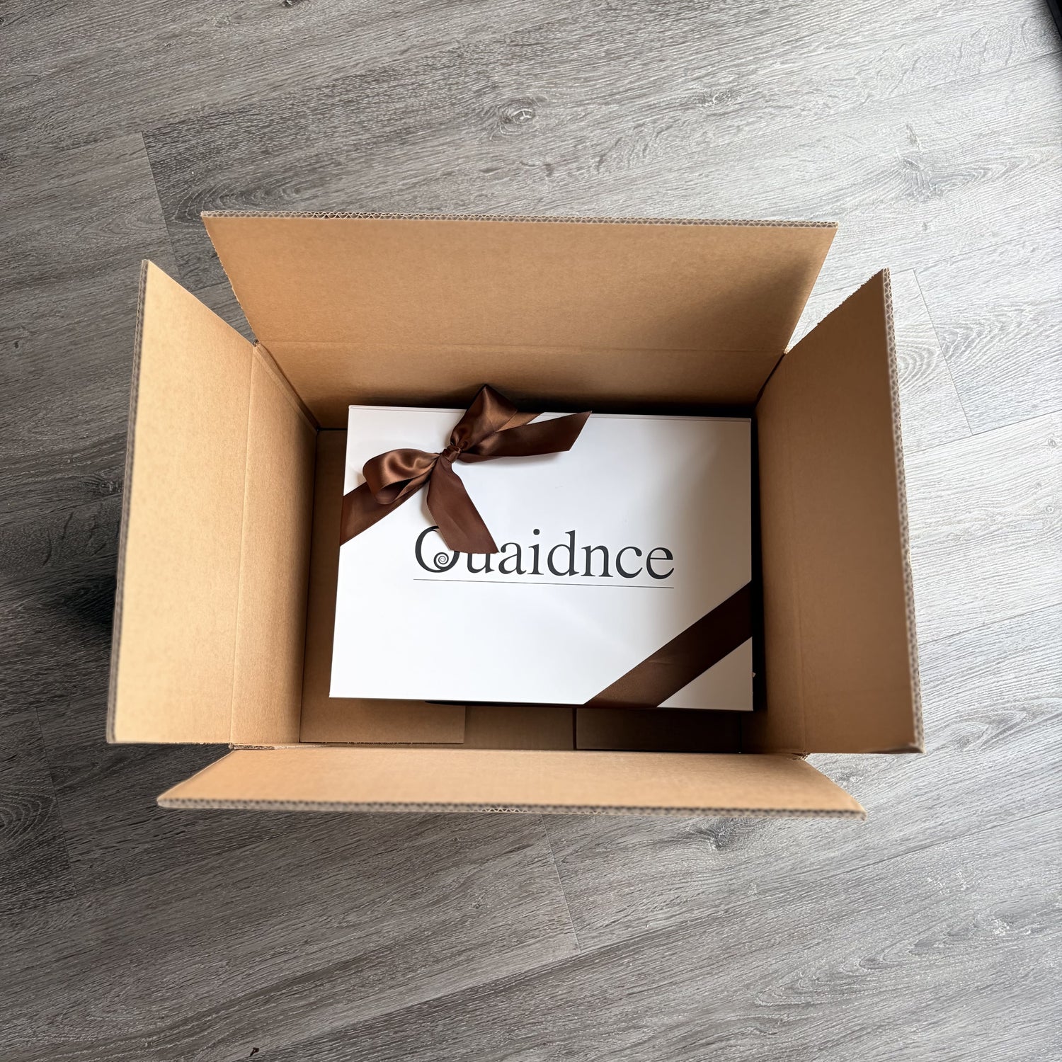 Open cardboard box with a white box inside featuring 'Quaidence' branding on a wooden surface.