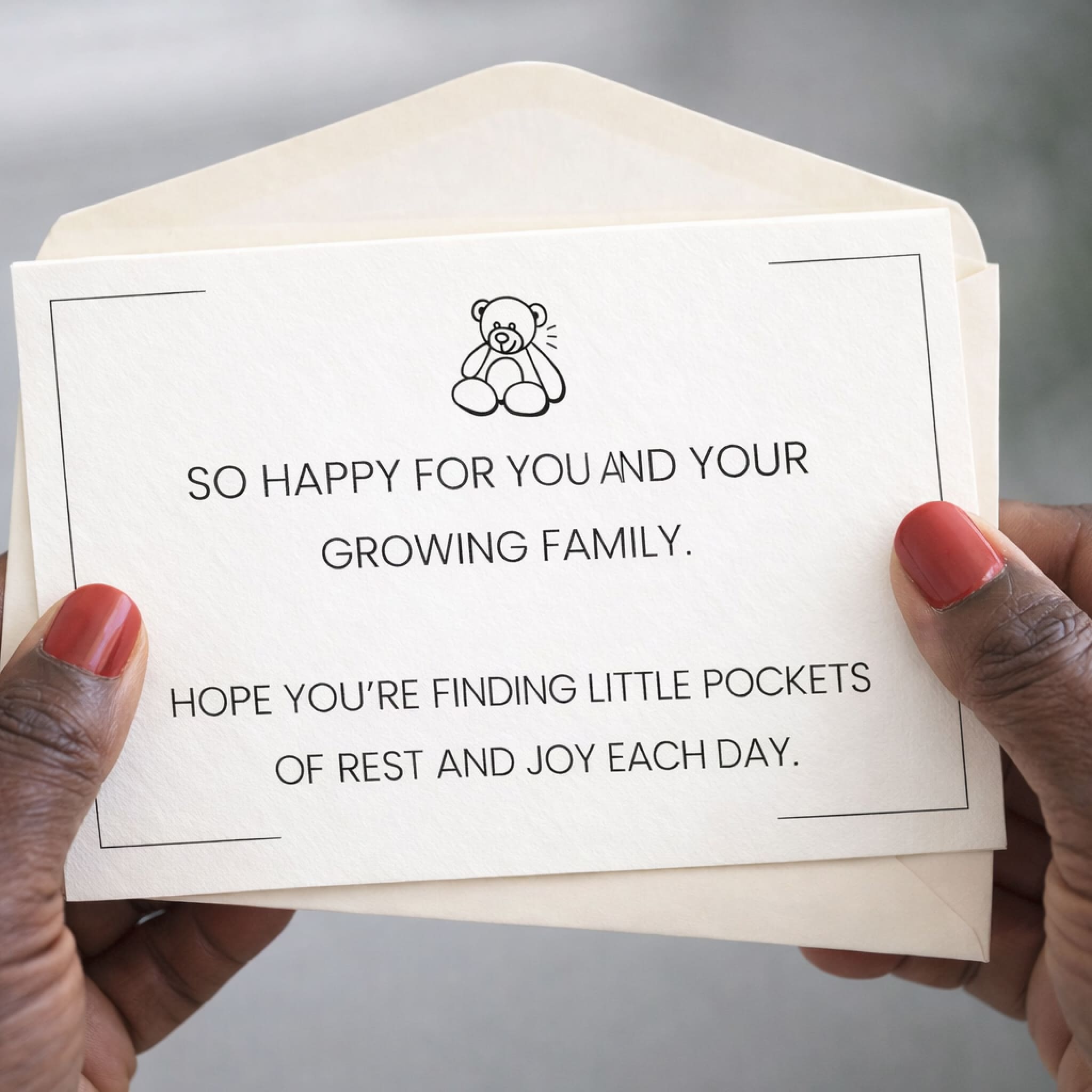Card with a message of congratulations for a growing family held by hands with red nail polish.