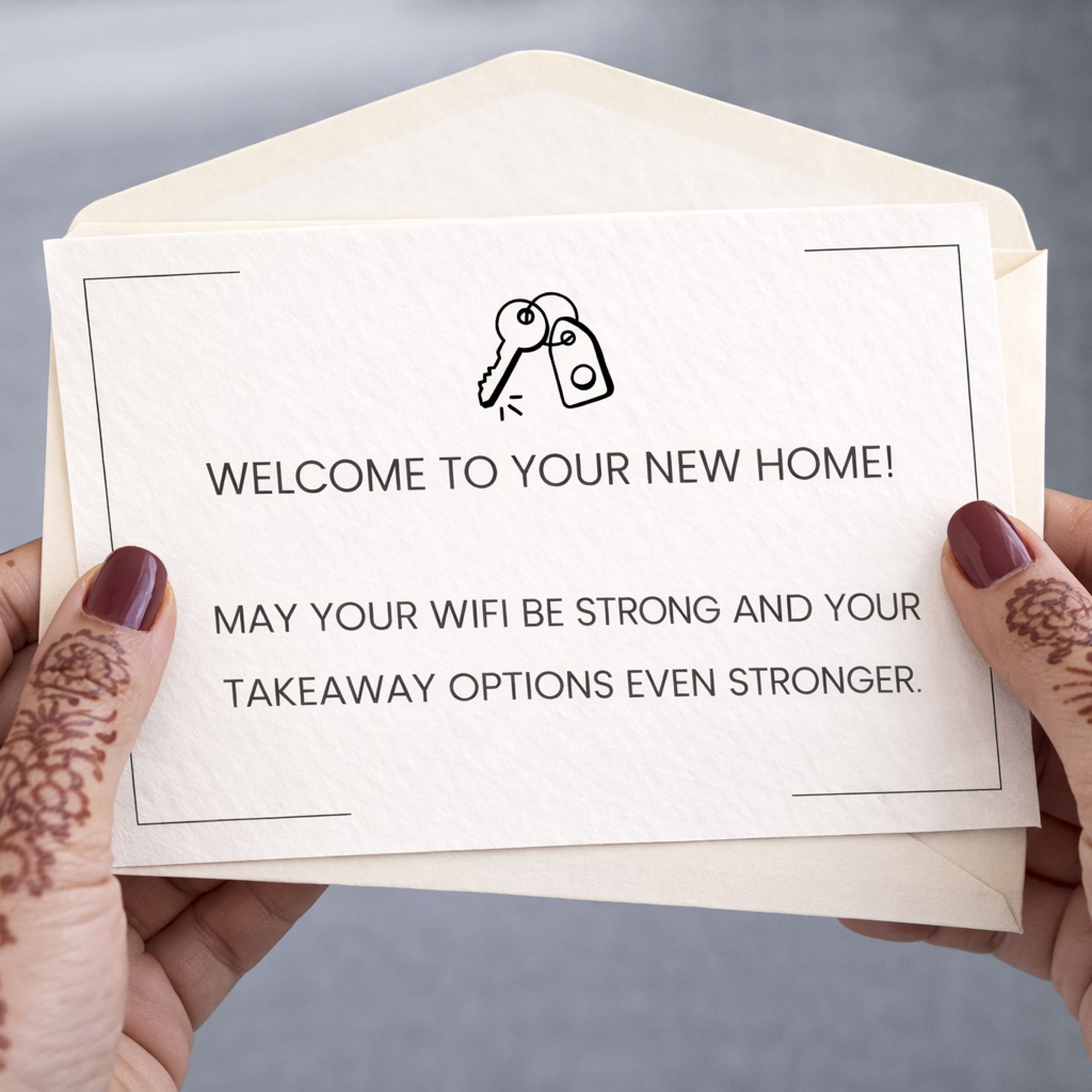 Card with humorous new home welcome message held by hands with henna designs.