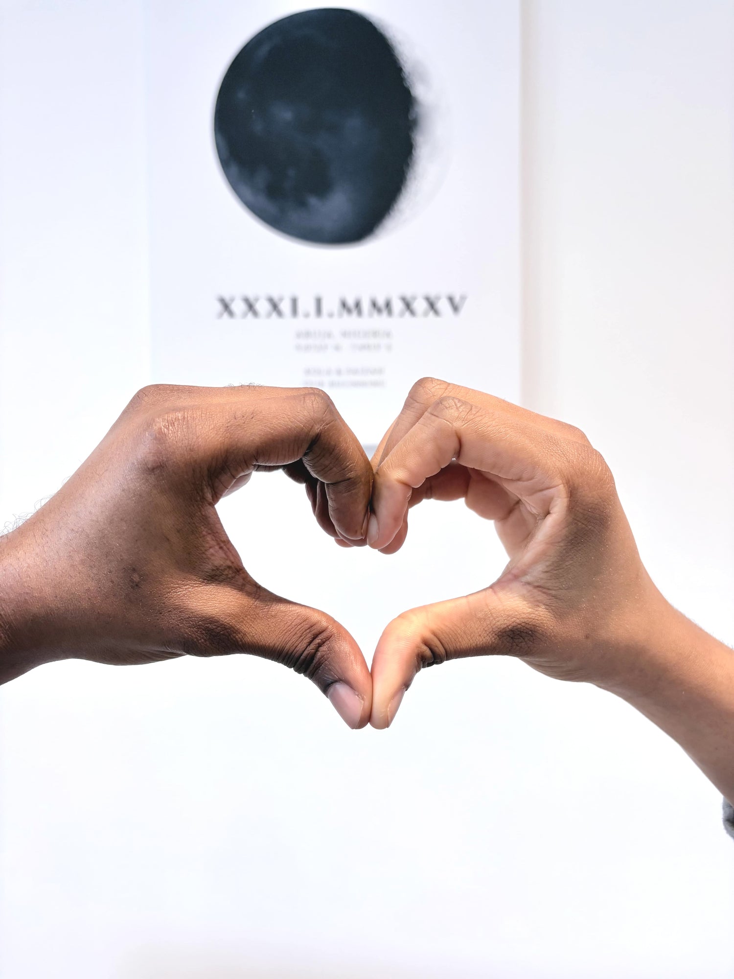 Two hands making a heart shape in front of a white background with a dark blue object and text.